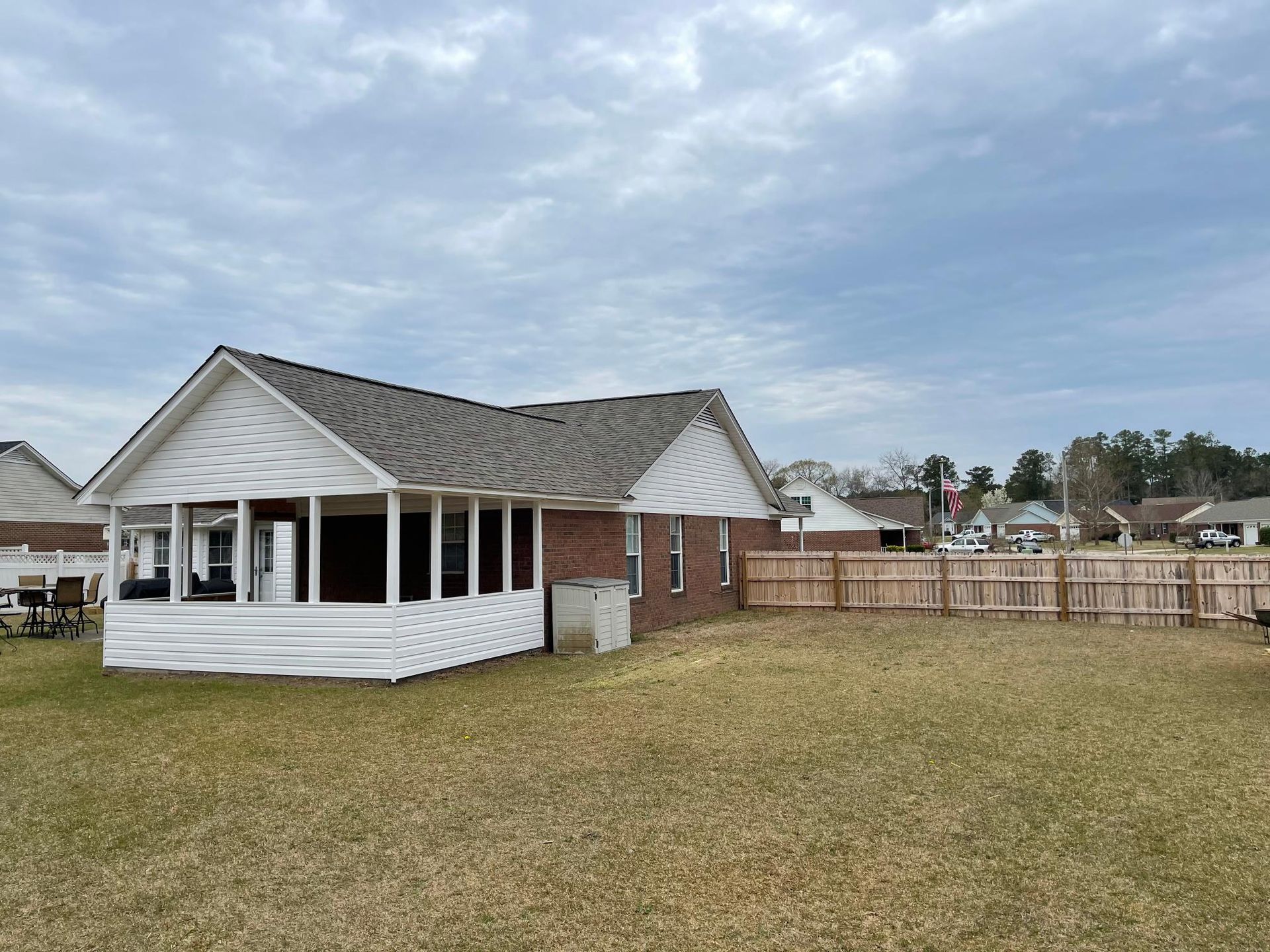 A small white house with a screened in porch is sitting in the middle of a grassy field.