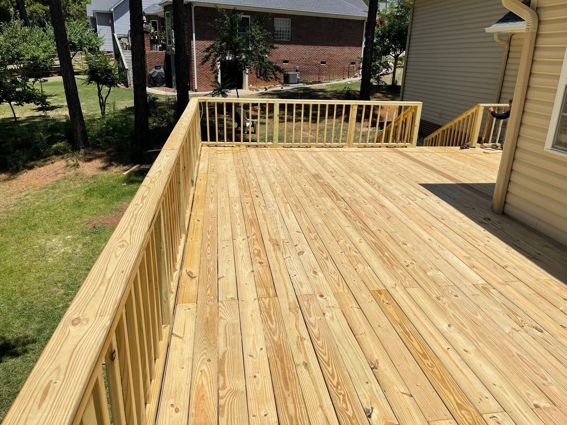 A large wooden deck with a railing is sitting next to a house.