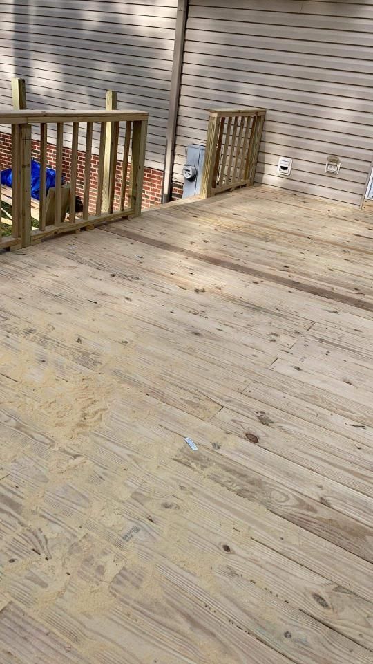 A wooden deck with a railing is being built in front of a house.