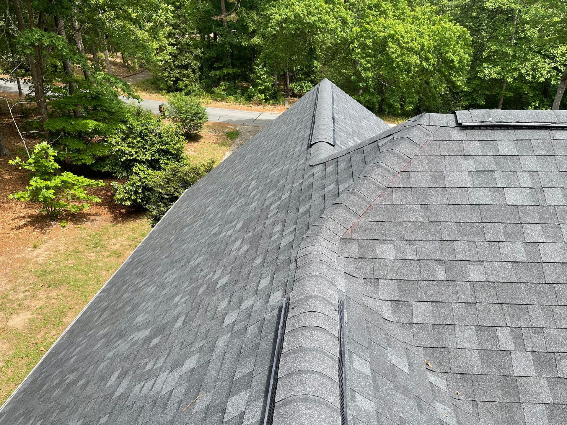 A roof with a lot of shingles is surrounded by trees and grass.