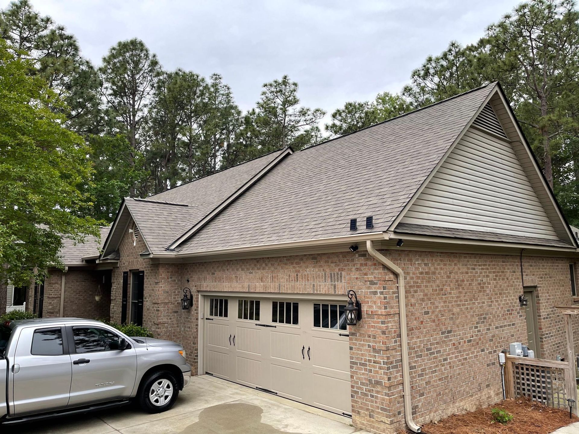 A silver truck is parked in front of a brick house with a garage door.
