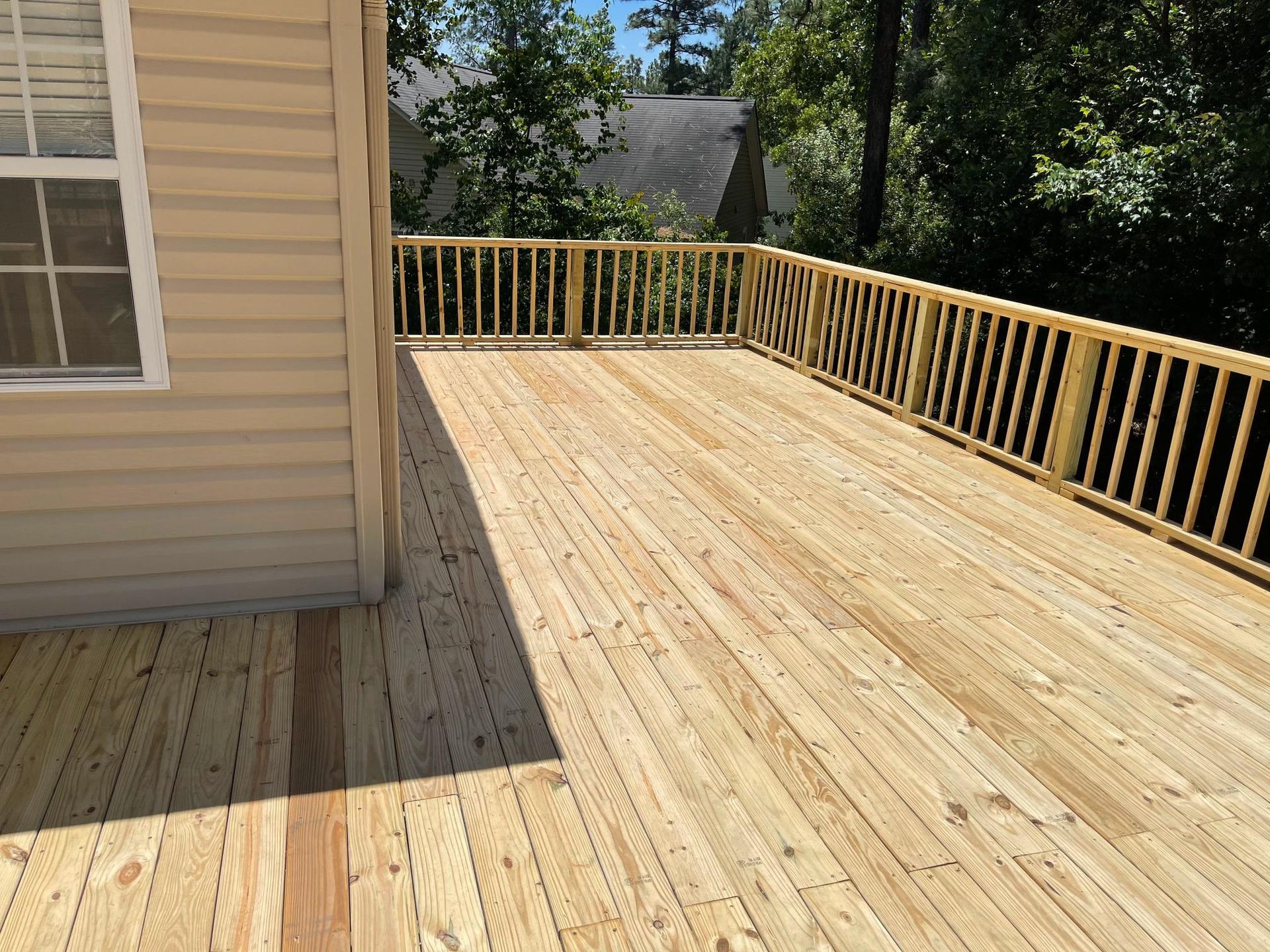 A large wooden deck with a railing is in front of a house.