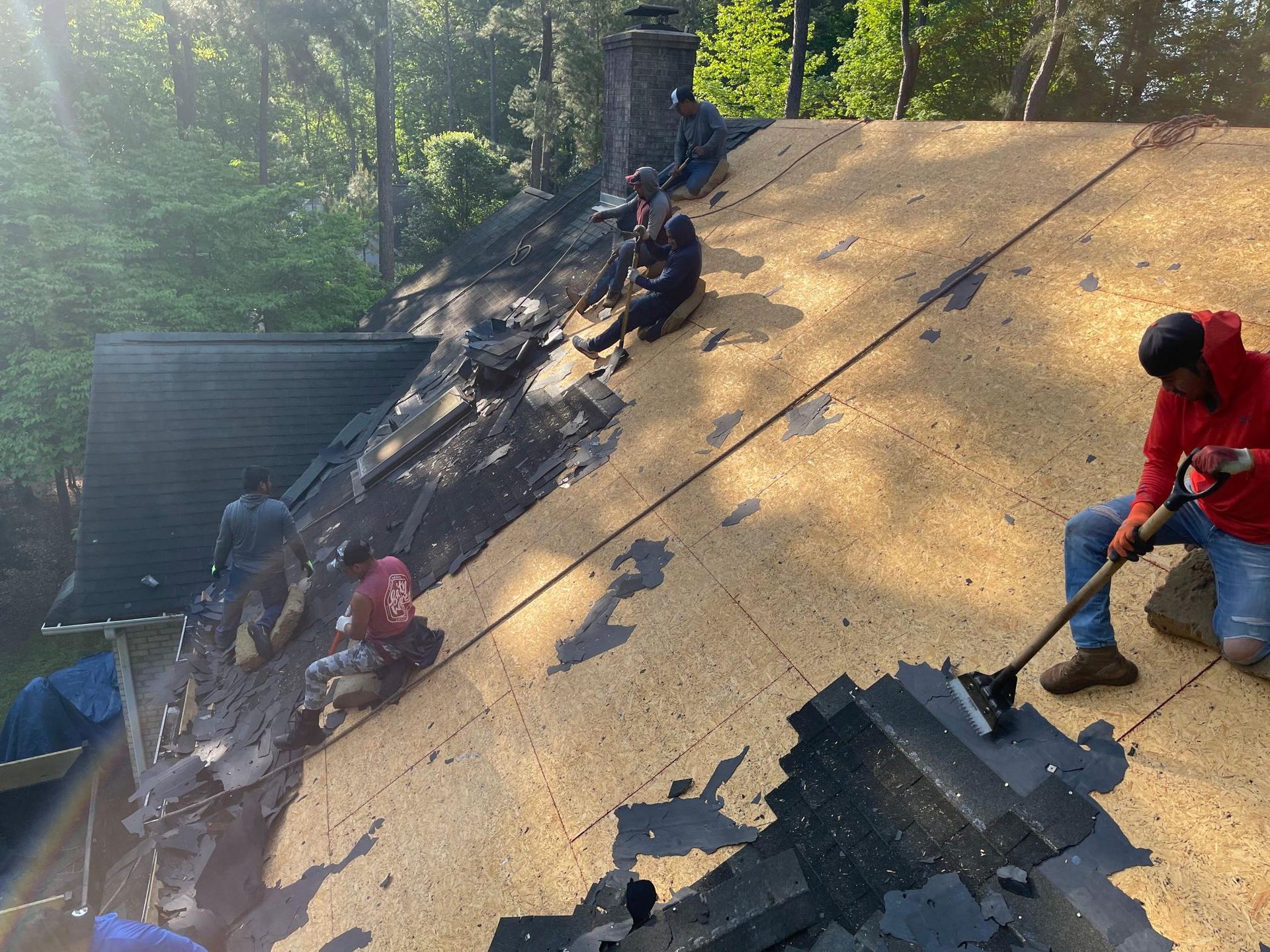 A man is sitting on top of a roof holding a rake.
