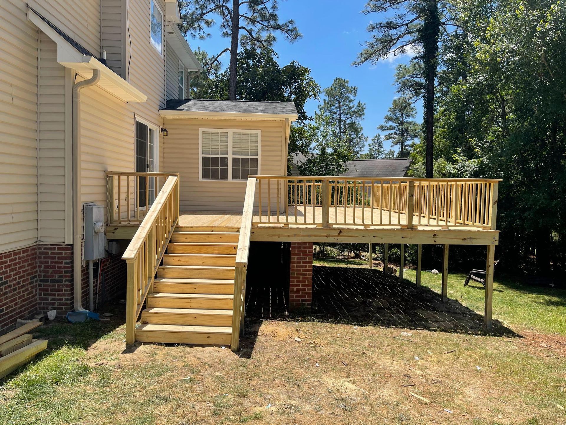 A wooden deck with stairs leading up to it is in the backyard of a house.