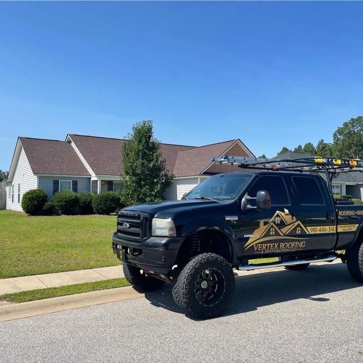 A black roofing truck is parked in front of a house