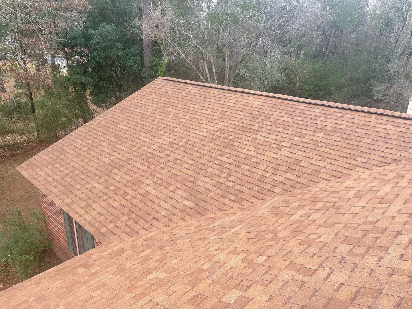 Brown shingled roof of a house, set amongst trees, angled view.