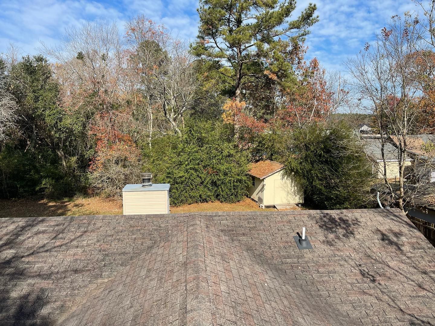 A roof with a chimney on it and trees in the background.