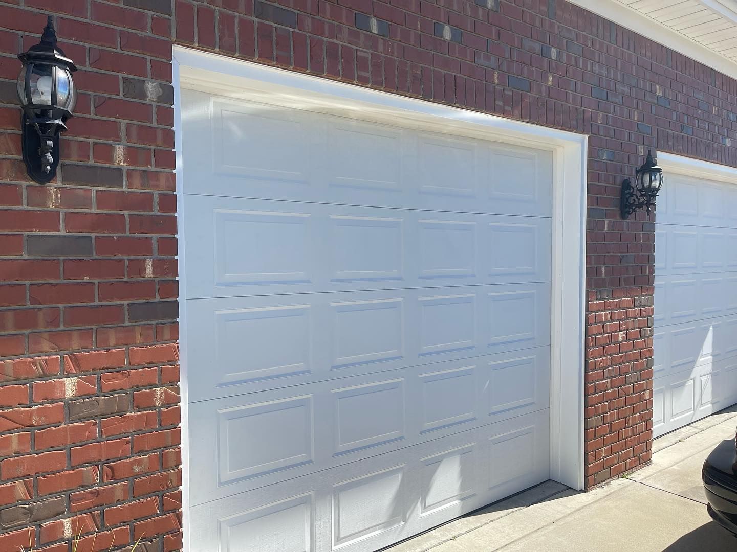 A car is parked in front of a brick building with white garage doors.