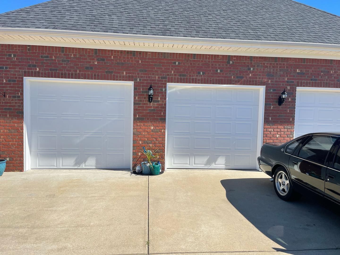 A car is parked in front of a garage with three white garage doors.