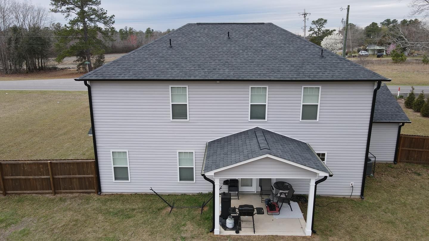 An aerial view of a white house with a gray roof and a porch.