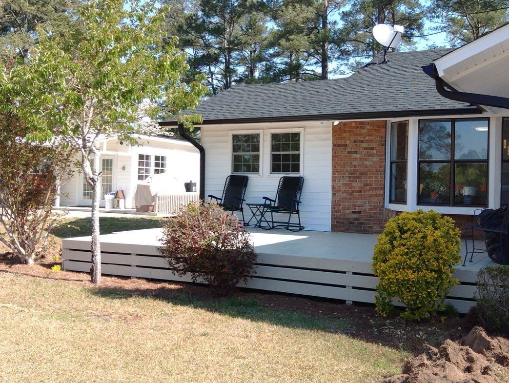 A white house with a porch and rocking chairs in front of it.