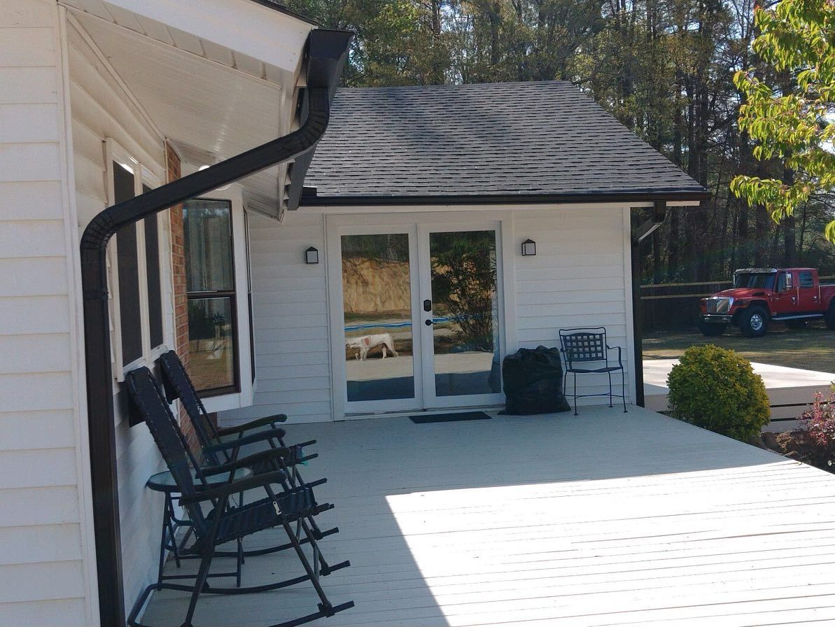 A white house with rocking chairs on the porch and a red truck parked in front of it.