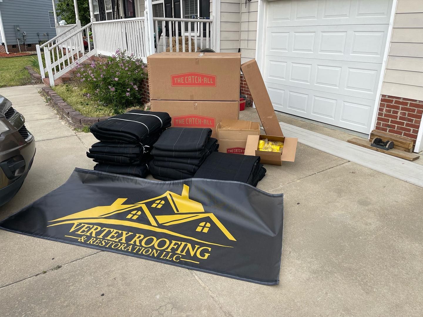 A banner for vertex roofing is sitting on the sidewalk in front of a garage.