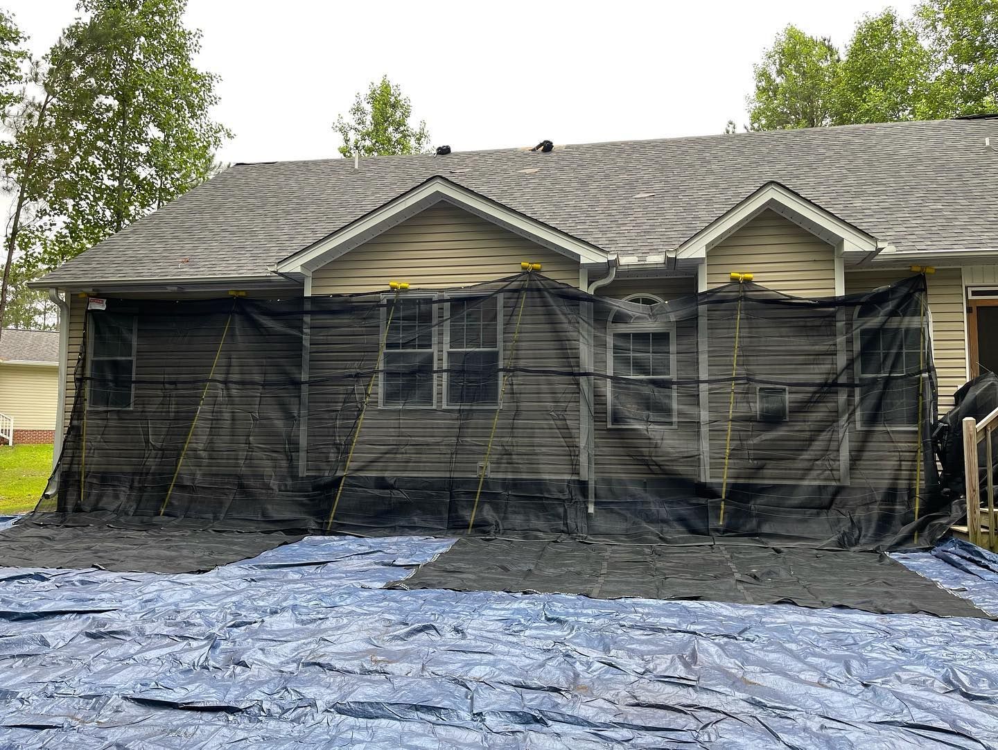 A house is covered in a tarp and is being painted.