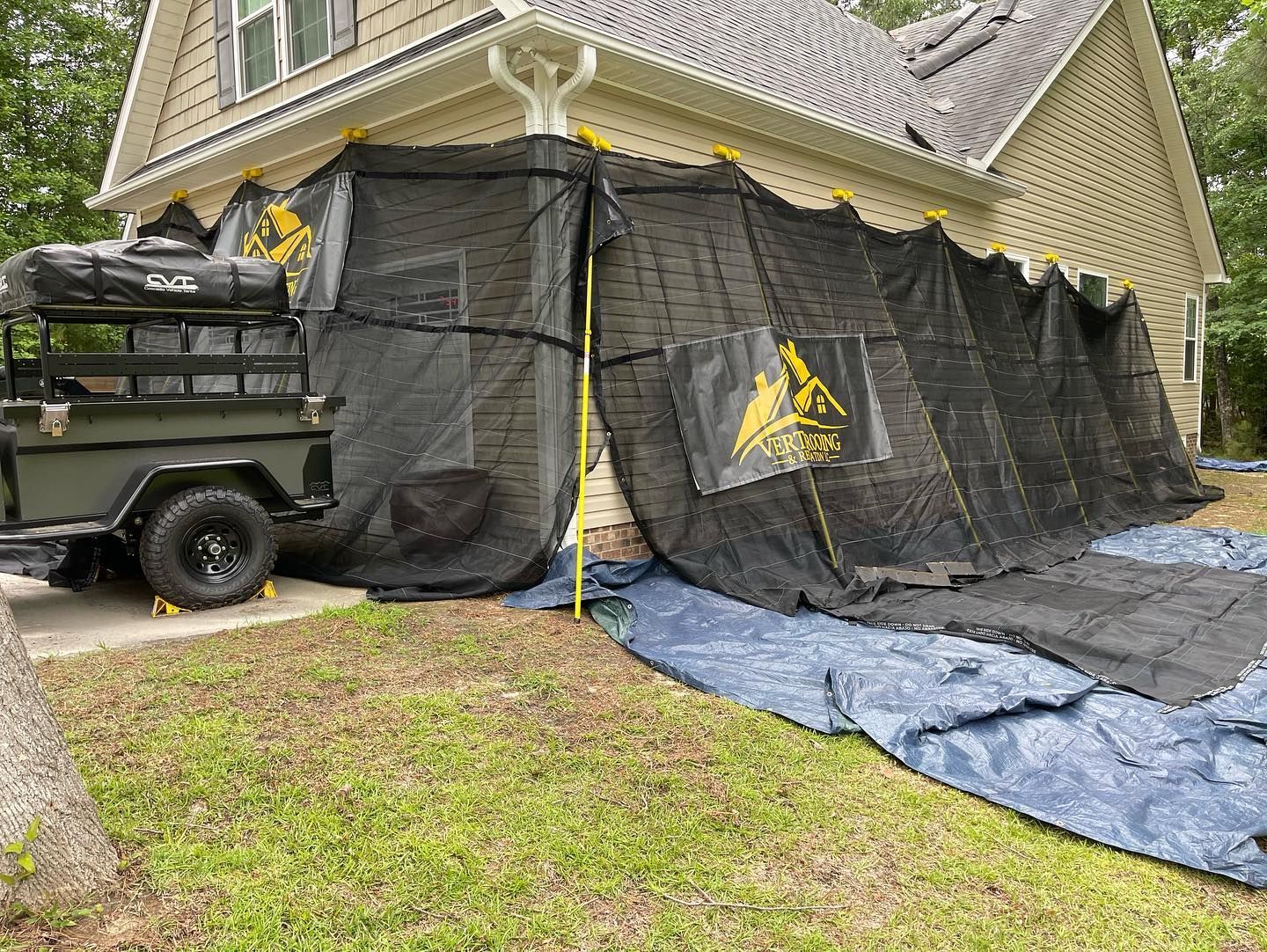 A trailer is parked in front of a house covered in tarps.