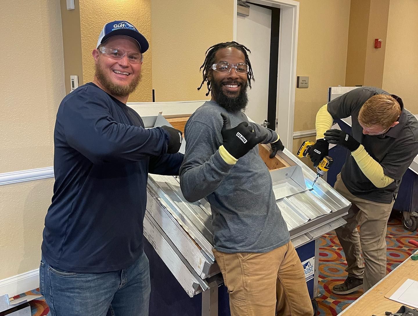 Three men are standing next to each other in a room holding a piece of metal.