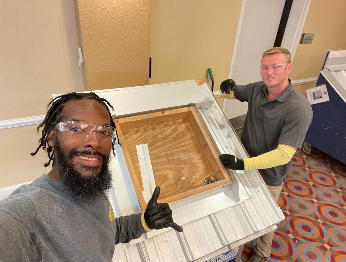 Two men are working on a piece of wood and one of them is giving a thumbs up.
