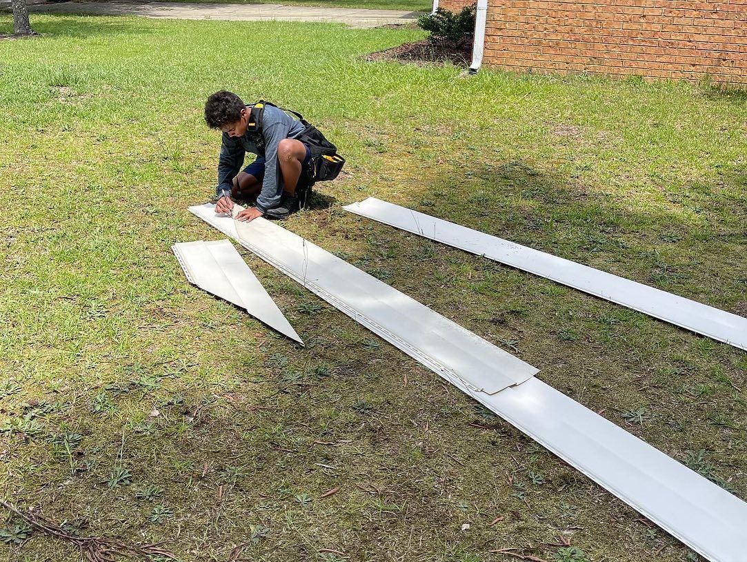 A young boy is kneeling on the grass cutting a piece of paper.