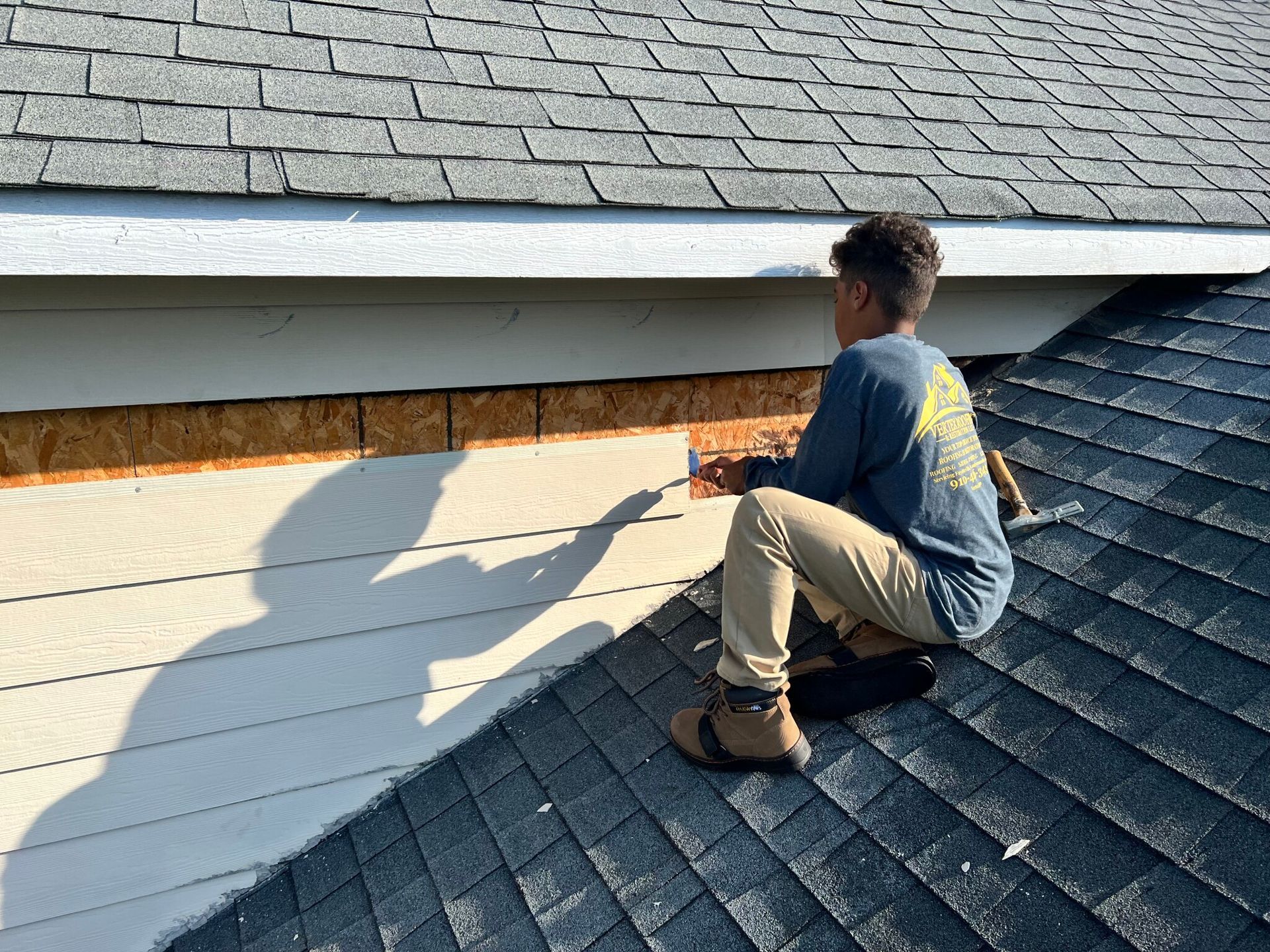 A man is kneeling on the roof of a house.