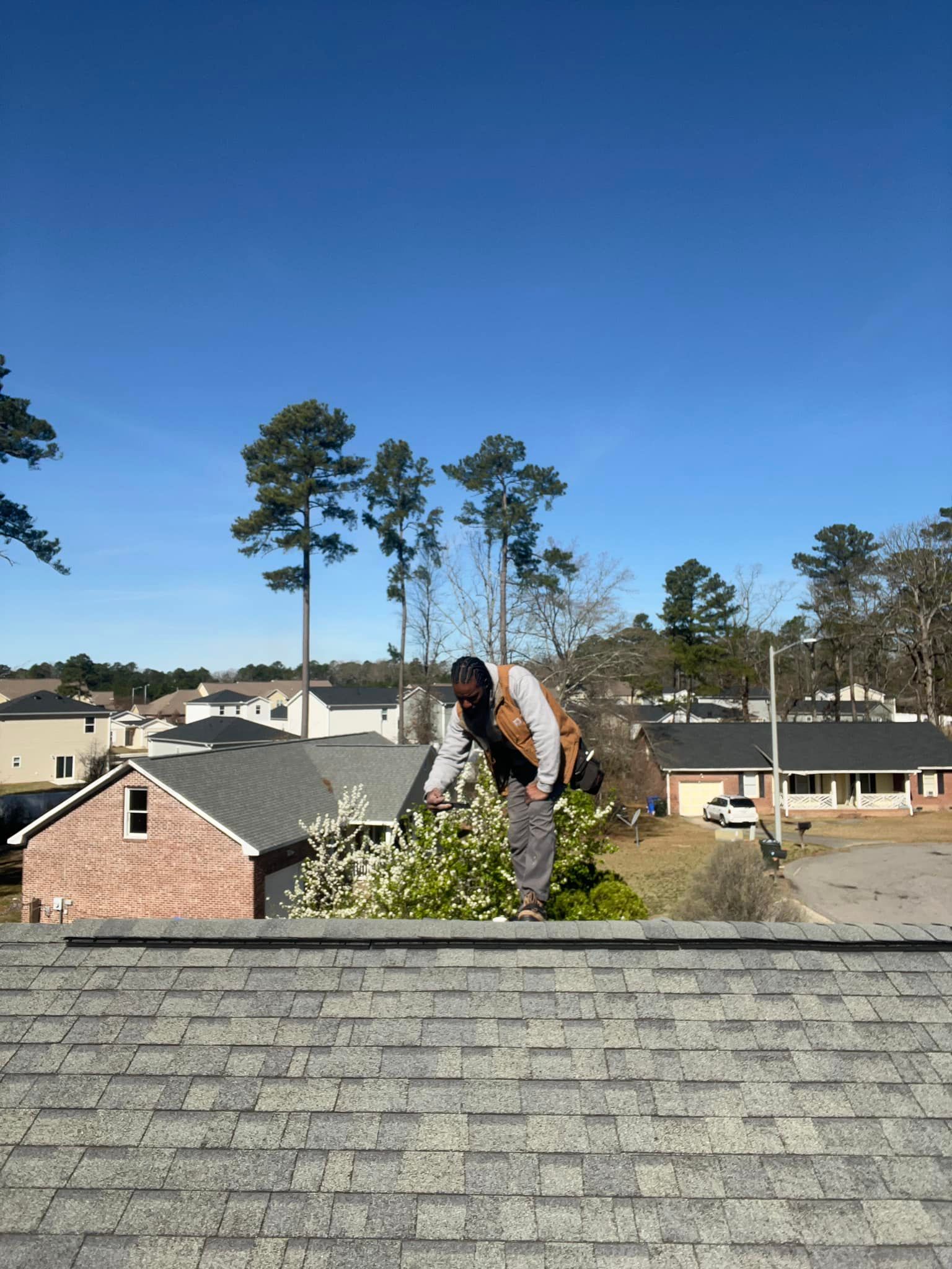 A man is standing on top of a roof cutting a tree.