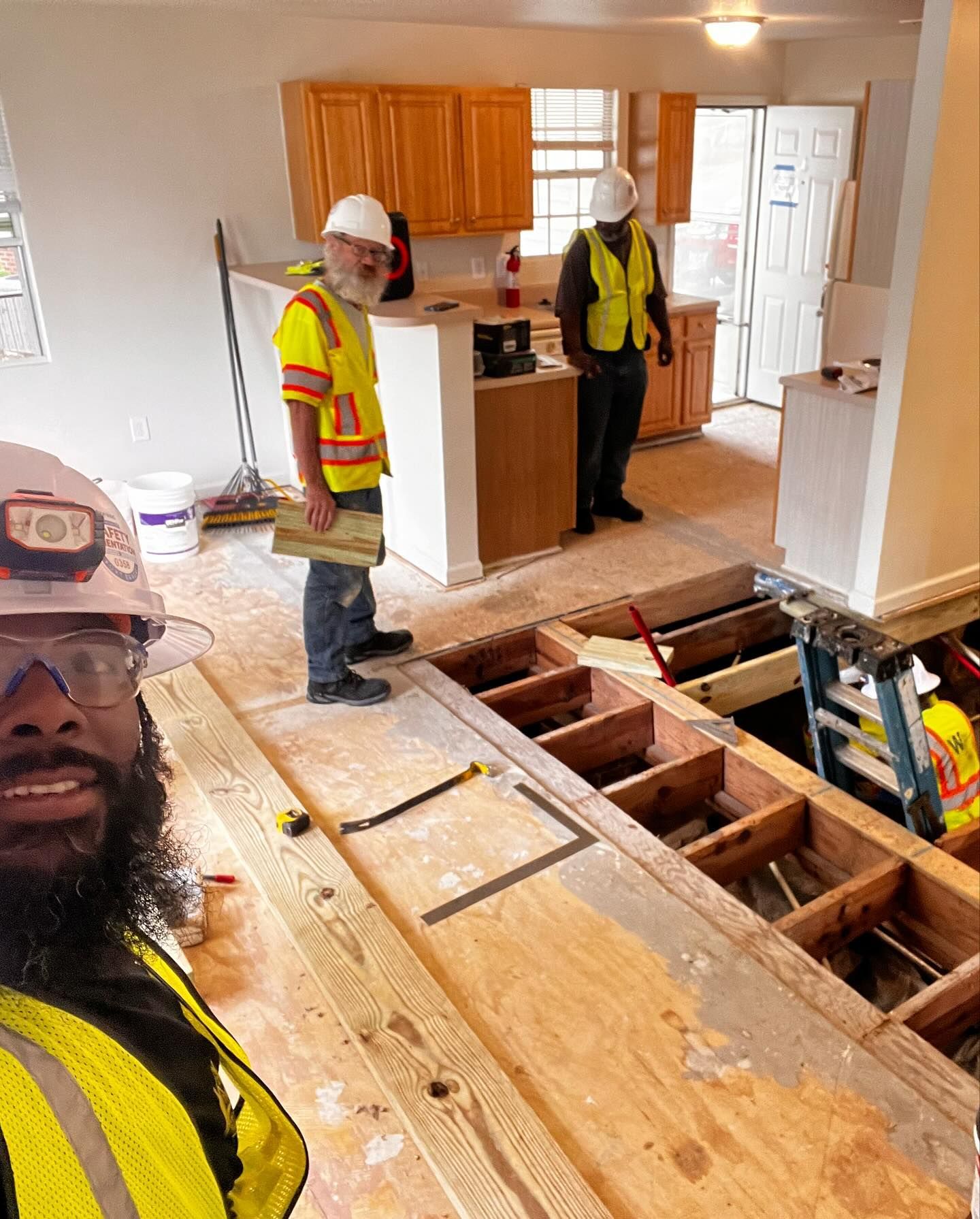 A man in a hard hat is standing on a wooden floor in a kitchen.