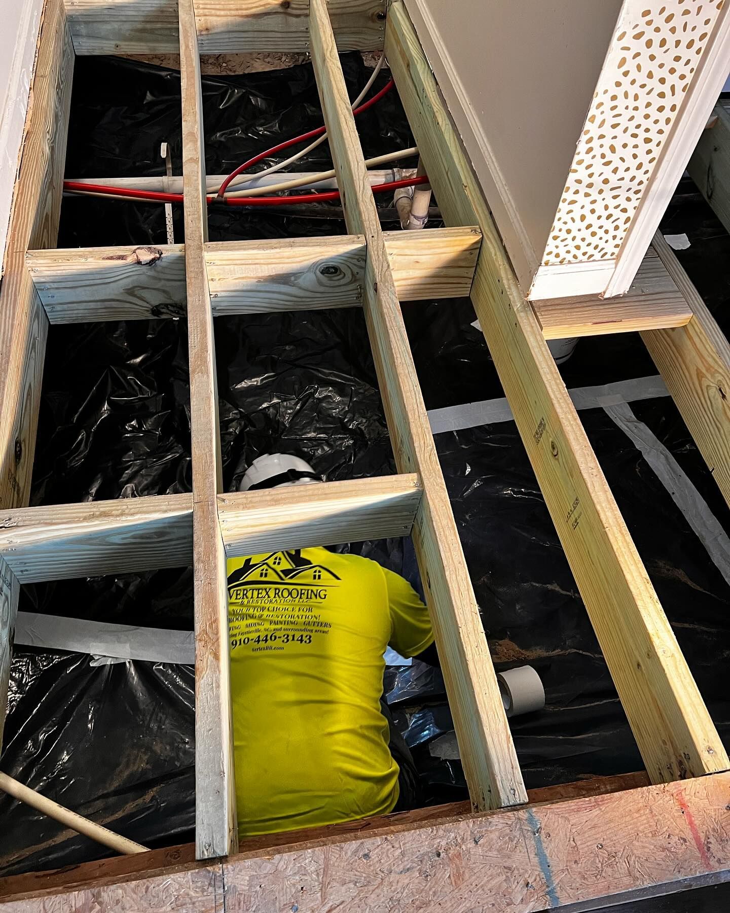 A man in a yellow shirt is working under a wooden floor.