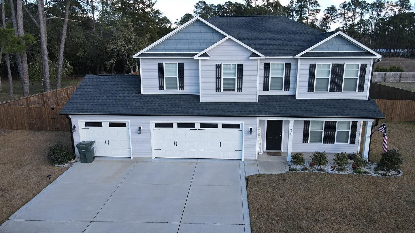 Two-story gray suburban house with attached three-car garage and wide concrete driveway