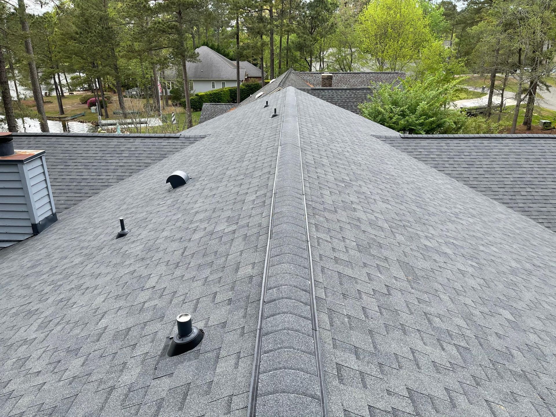 A close up of a roof with a chimney and trees in the background.