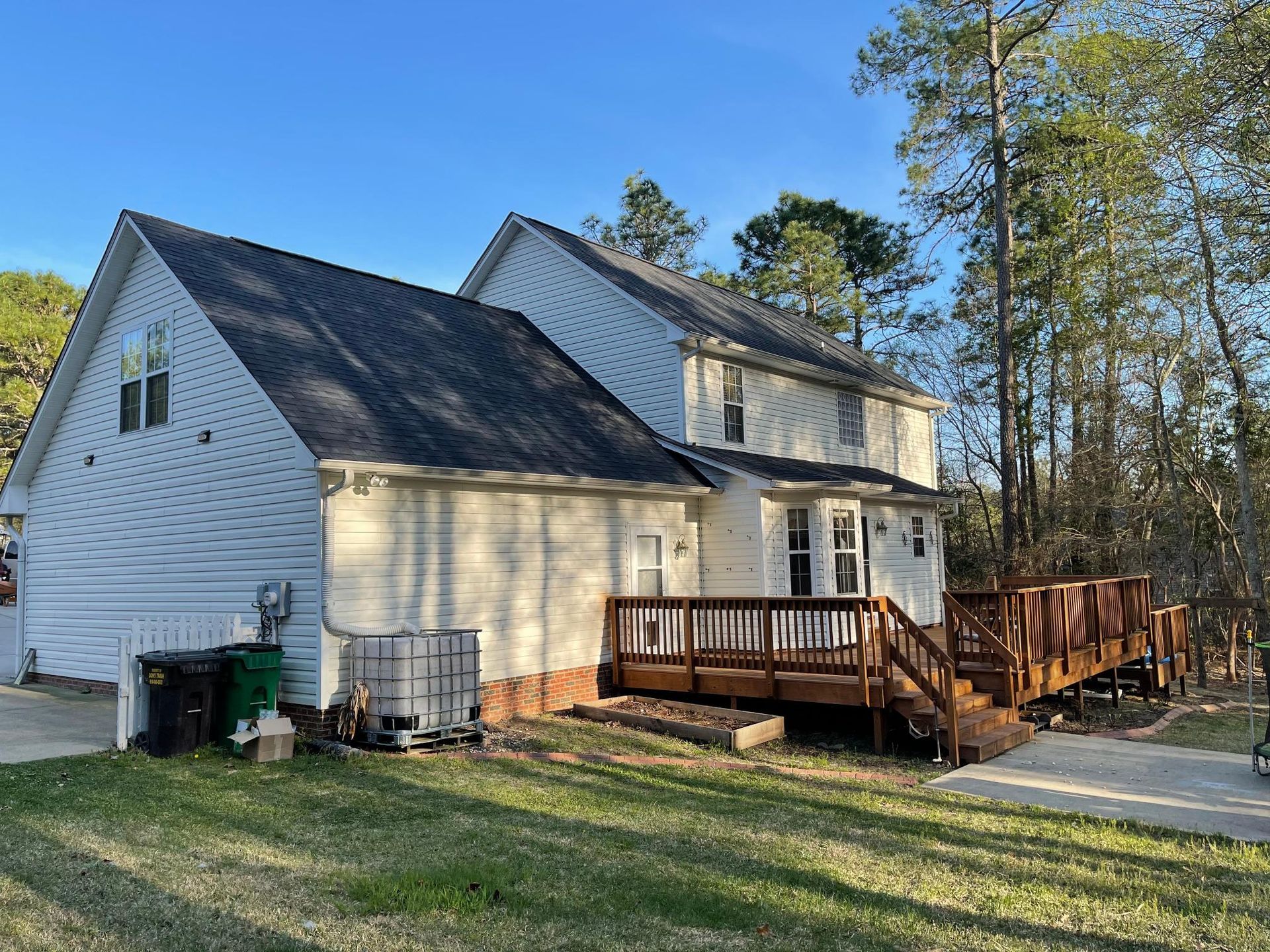 A white house with a black roof and a wooden deck surrounded by trees.