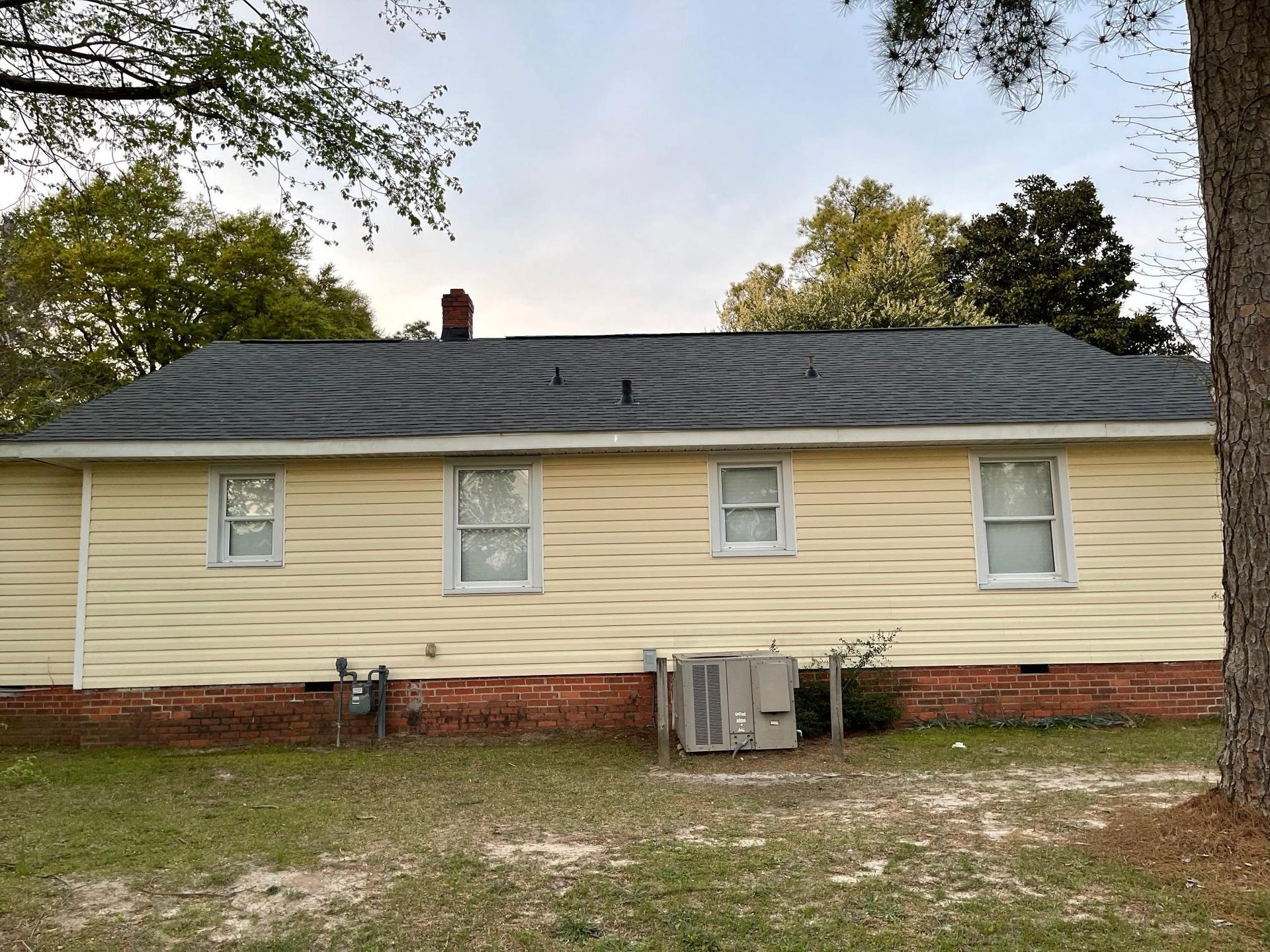 A yellow house with a black roof and a tree in front of it
