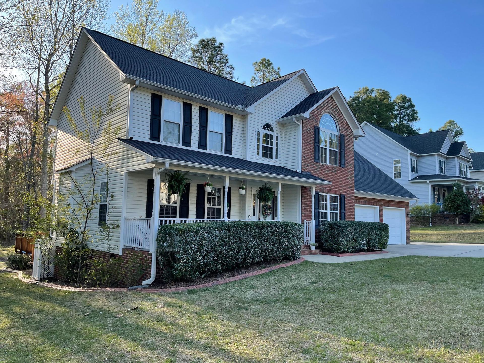 A large white house with a black roof is sitting on top of a lush green field.