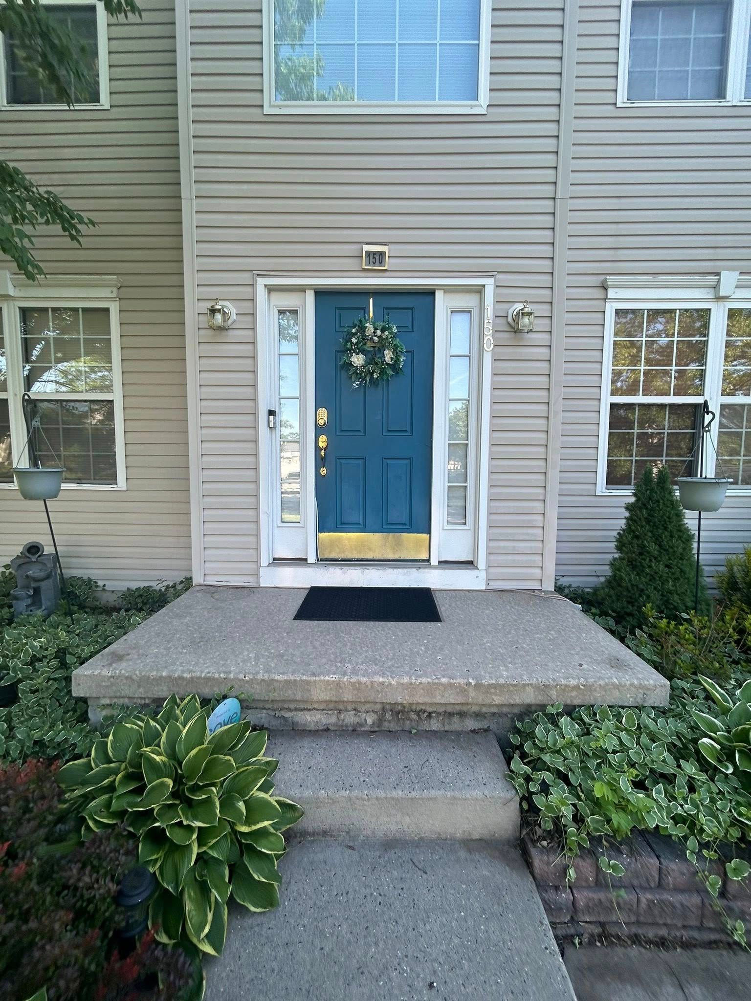 Tan house with teal door, wreath, and concrete steps.