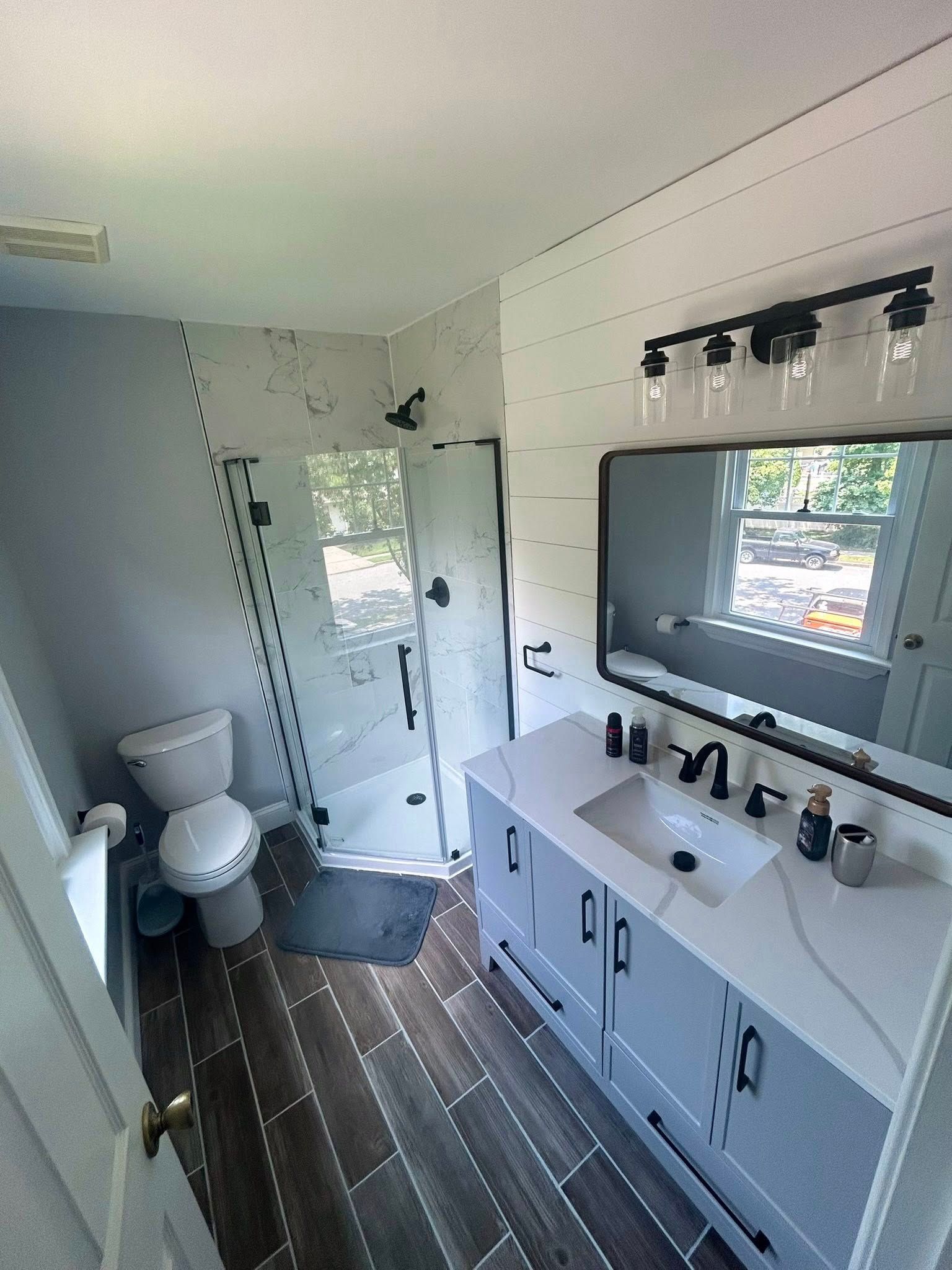 Modern bathroom with gray vanity, shower, toilet, and wood-look tile.