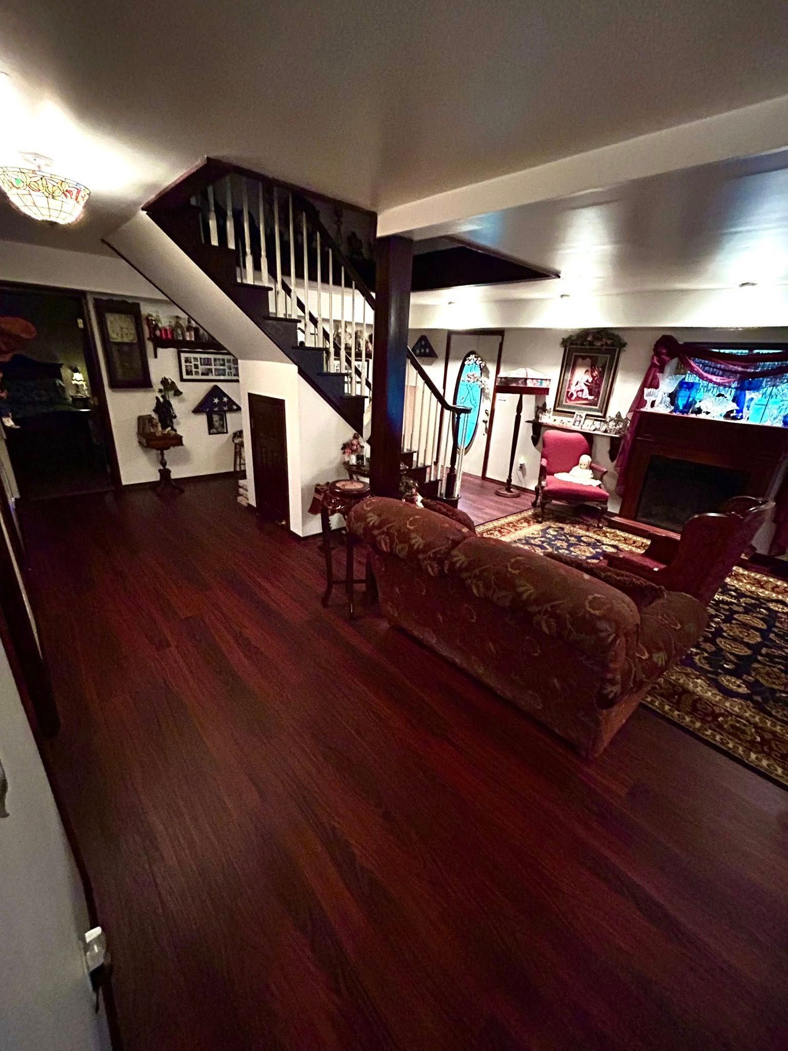 Dark wood-floored room with staircase, red sofa, and arcade game.