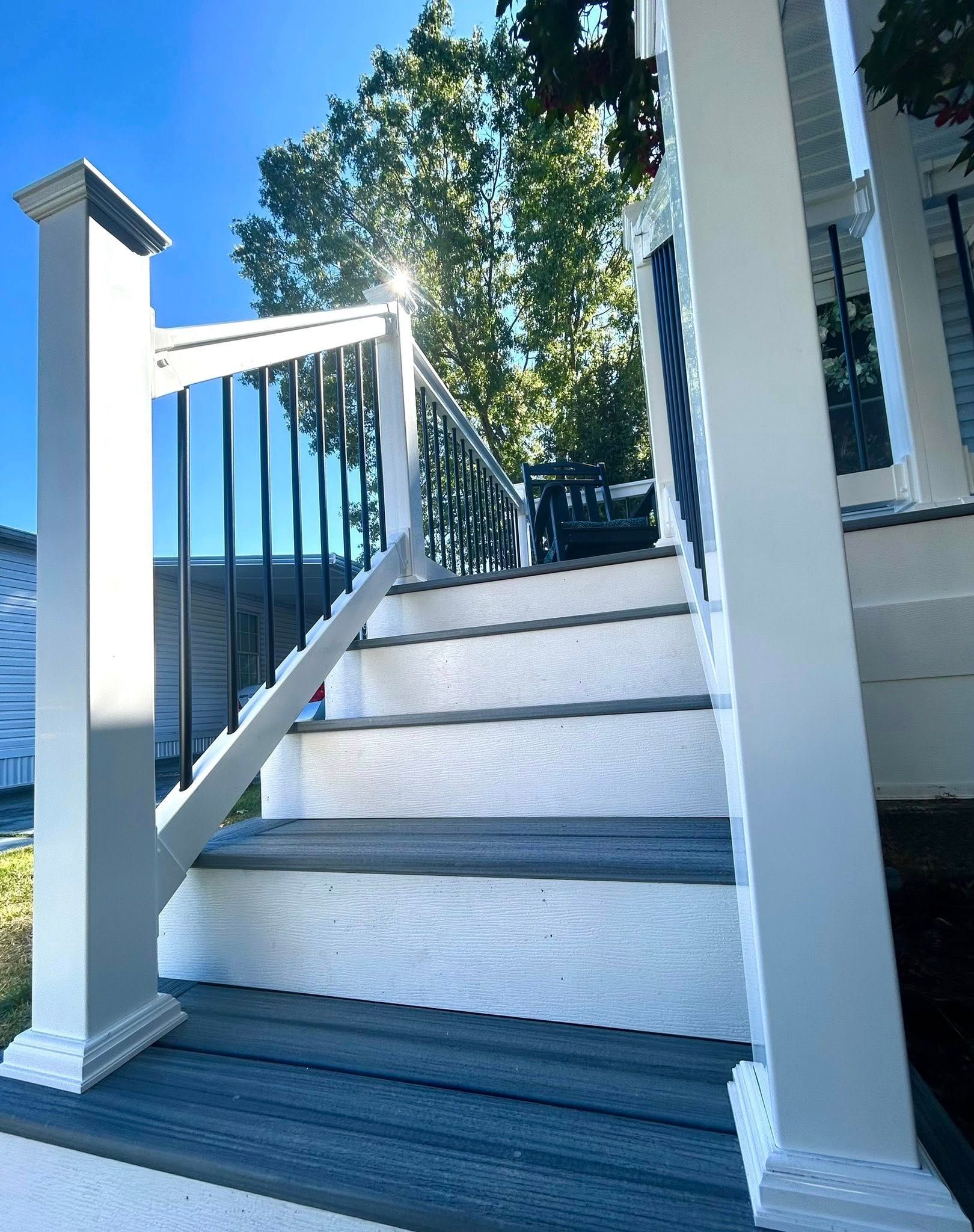 Exterior staircase with white and gray steps, black railing, leading up to a house.