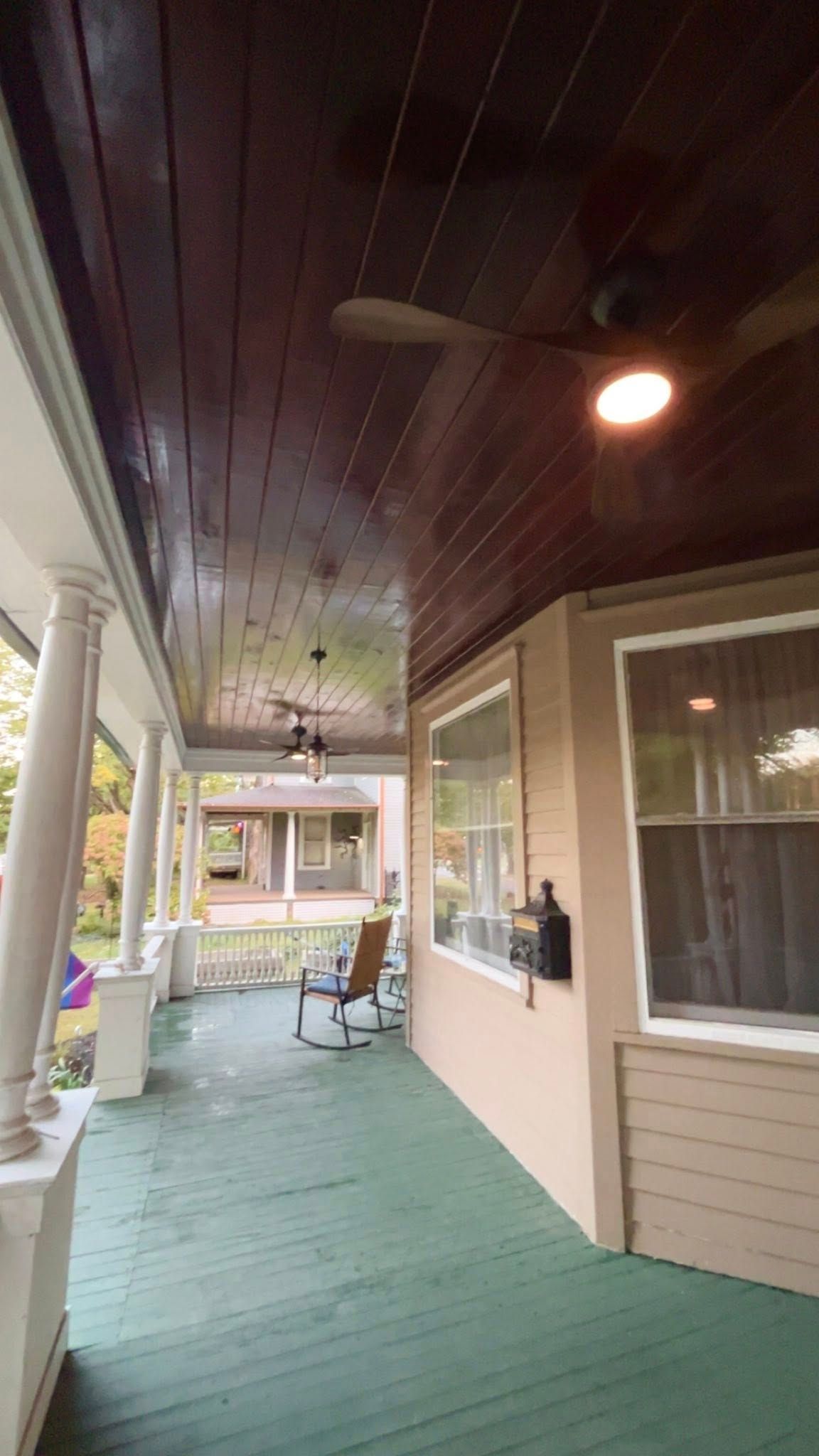 Porch with dark wood ceiling, green floor, white columns, and beige siding.