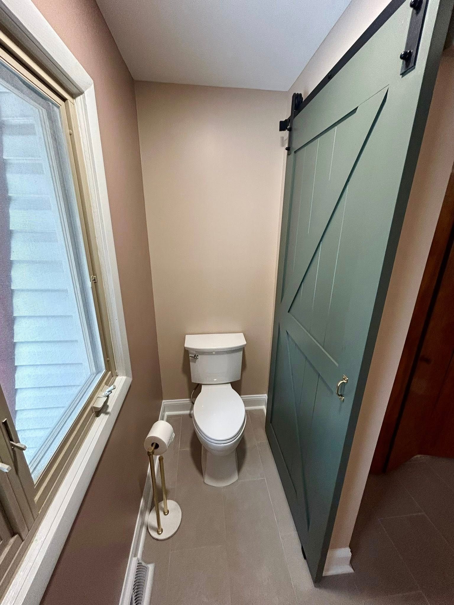 Small bathroom with a toilet, window, and sliding barn door.