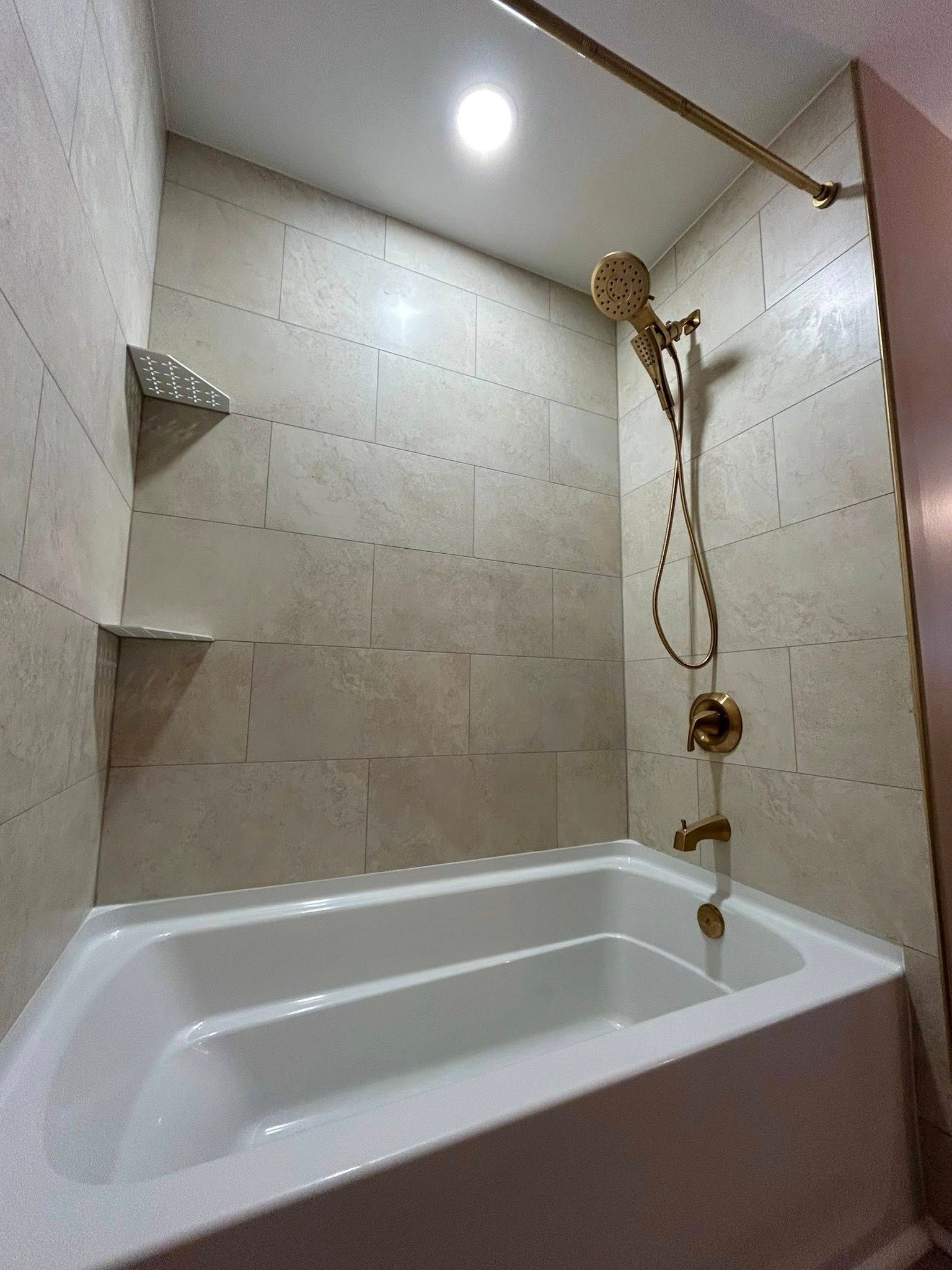 Bathroom with white bathtub, gold showerhead, and tiled walls.
