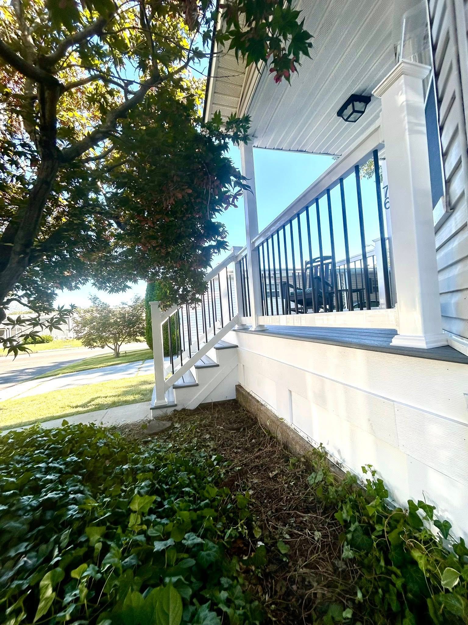 White porch with black railing and steps, green bushes in front.