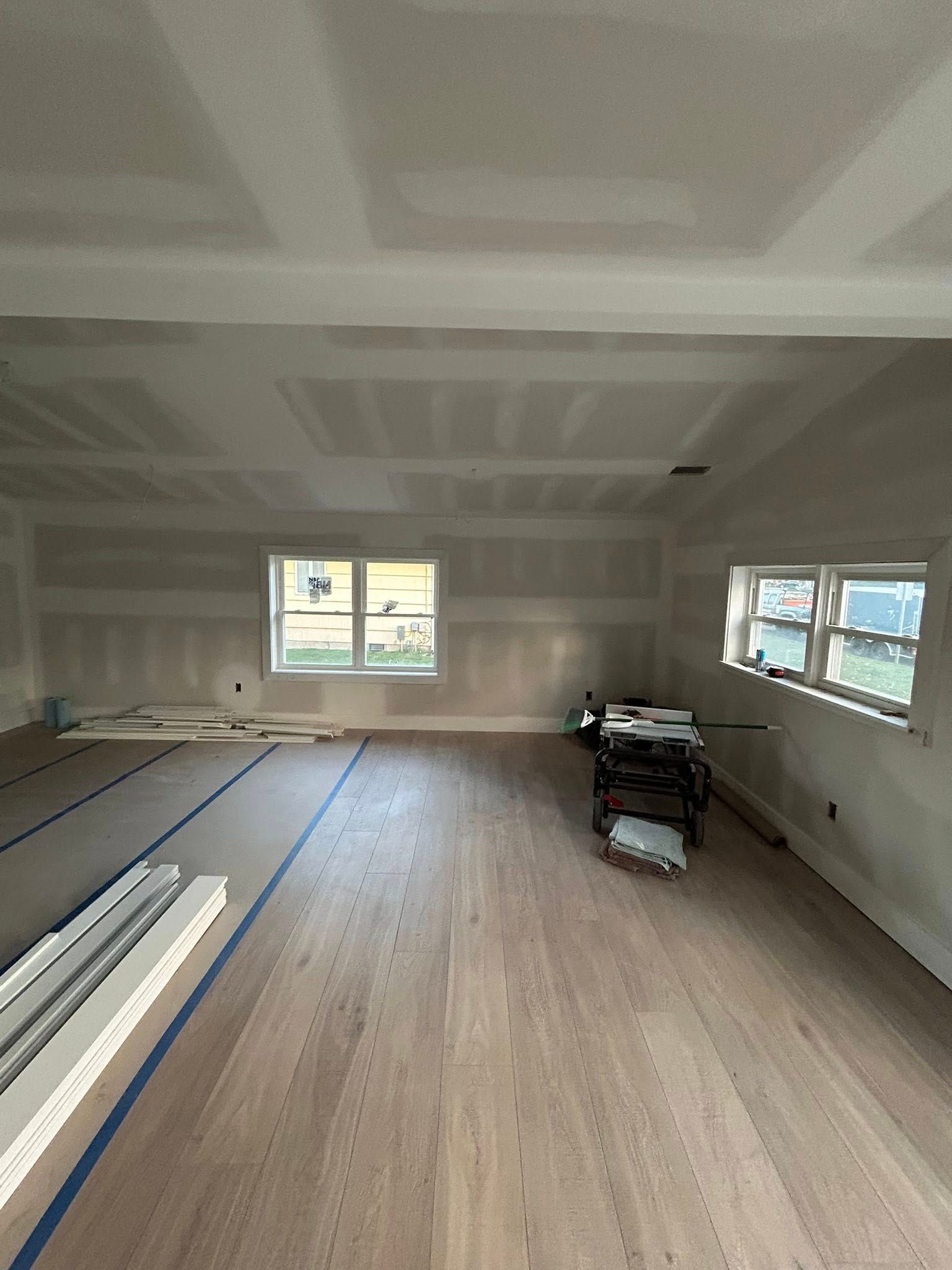 Interior room under construction, with drywall, wood flooring, and windows.
