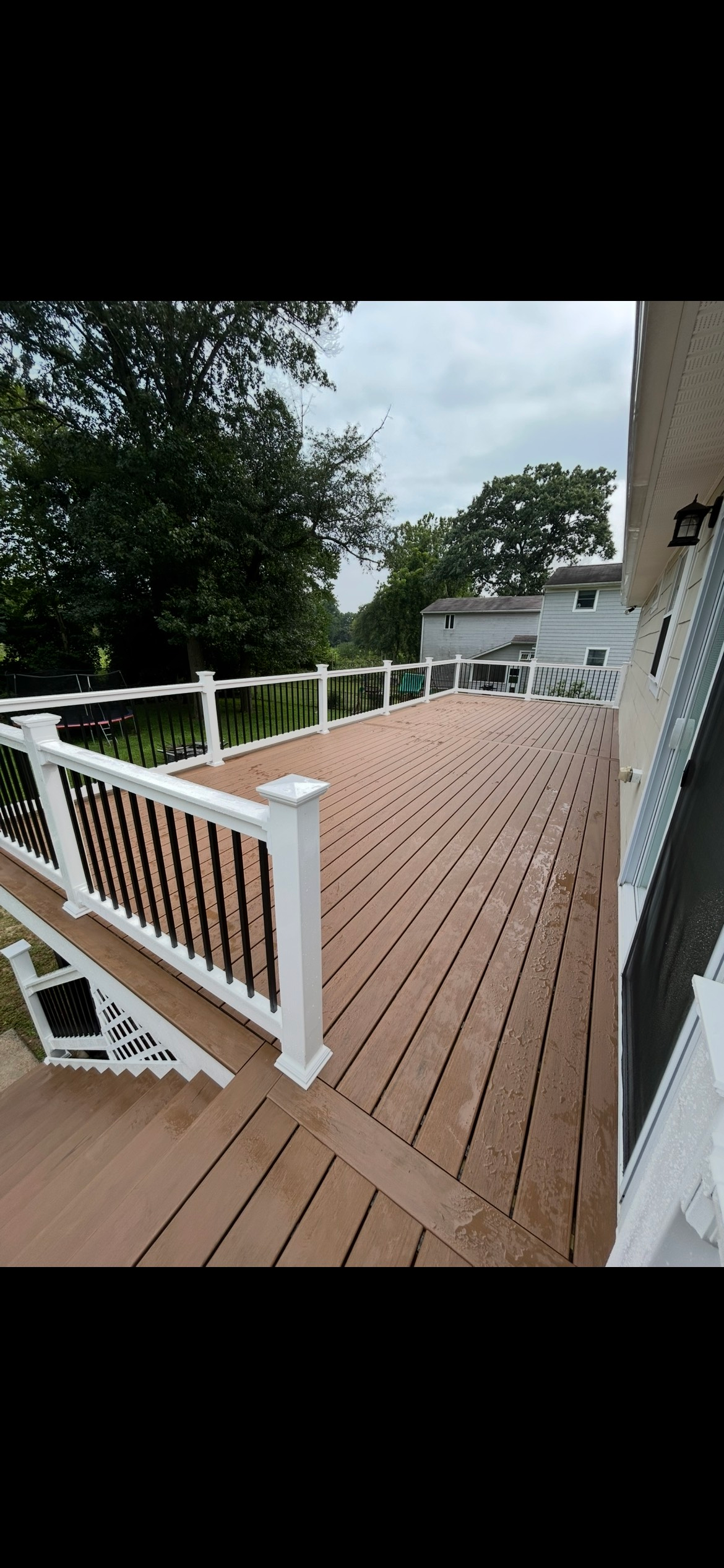 Grey composite deck surrounds a blue pool, white fence and cloudy sky in the background.