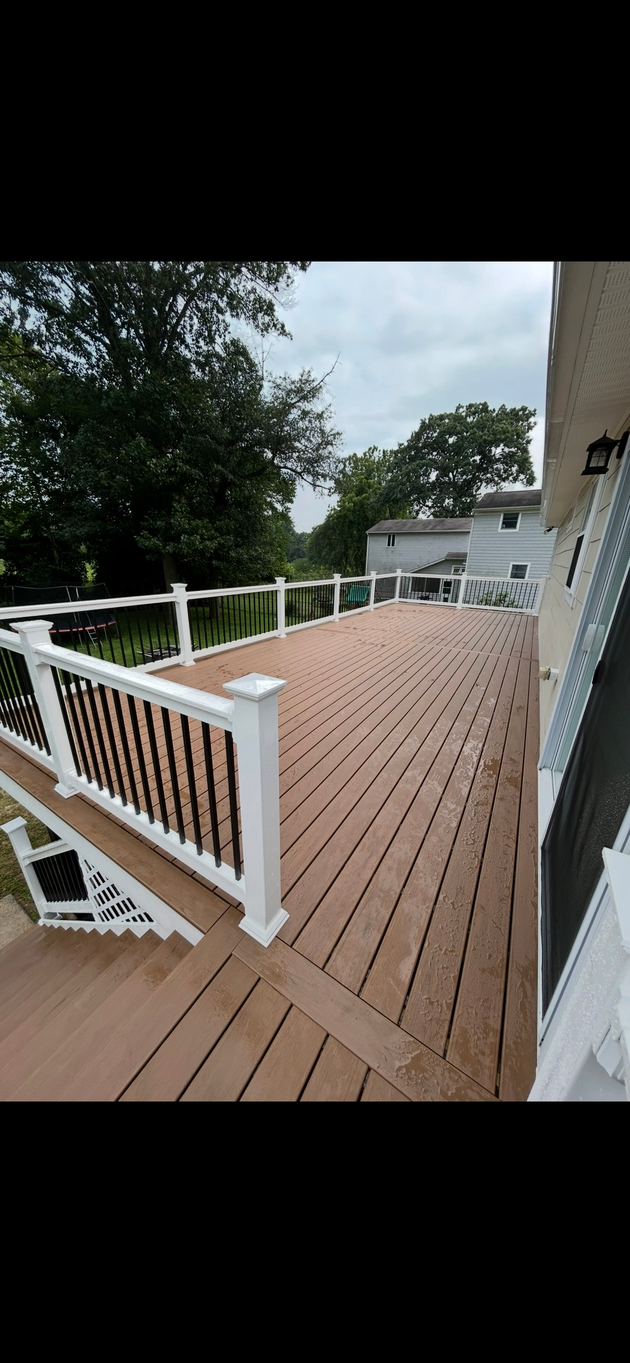 Grey composite deck surrounds a blue pool, white fence and cloudy sky in the background. Grey composite deck surrounds a blue pool, white fence and cloudy sky in the background.