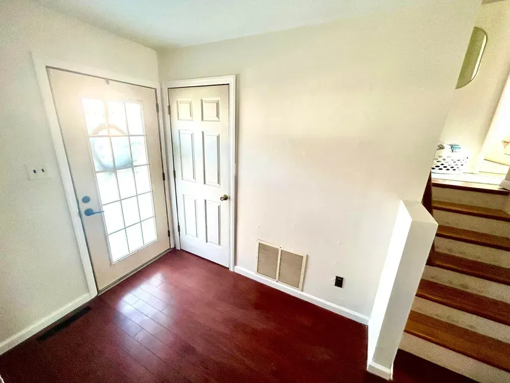 Entryway with burgundy floor, white doors, and a staircase.