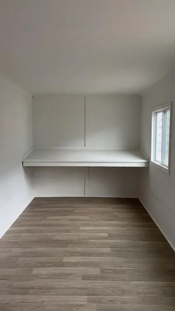 Empty room with white walls, a floating desk, and wood-look flooring.