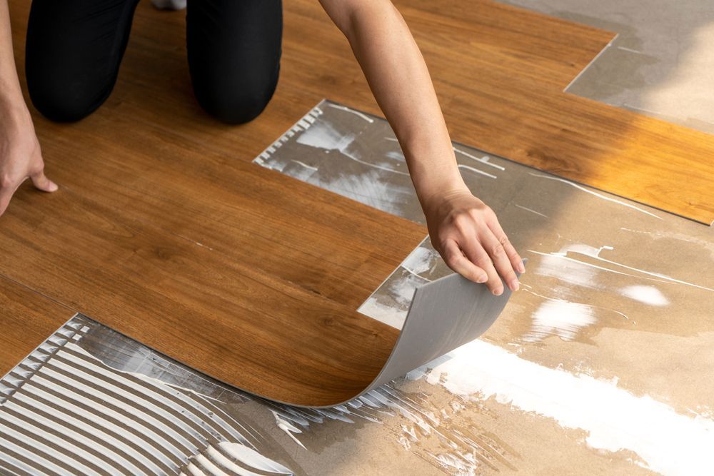 A person is laying a piece of vinyl flooring on a wooden floor.