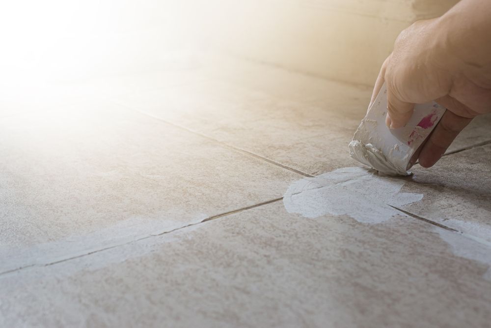 A person is applying grout on a tile floor with a sponge.