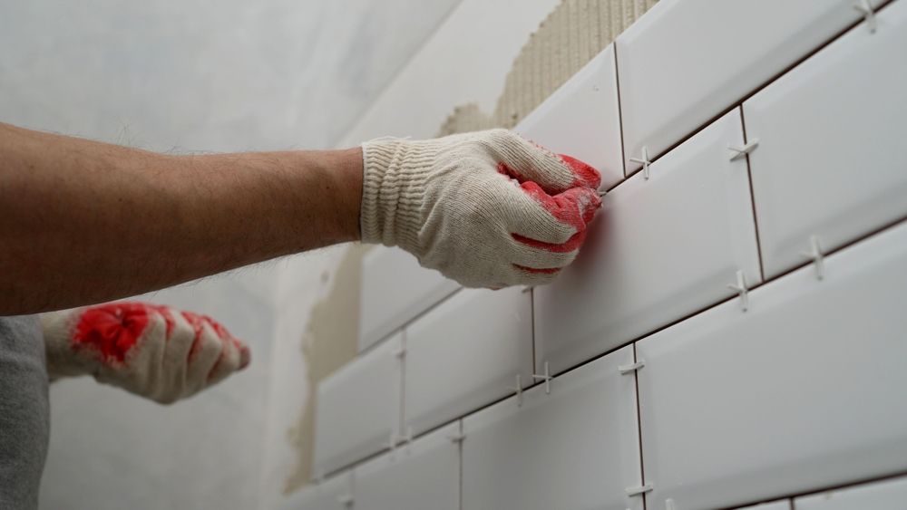 A man is installing white tiles on a wall.