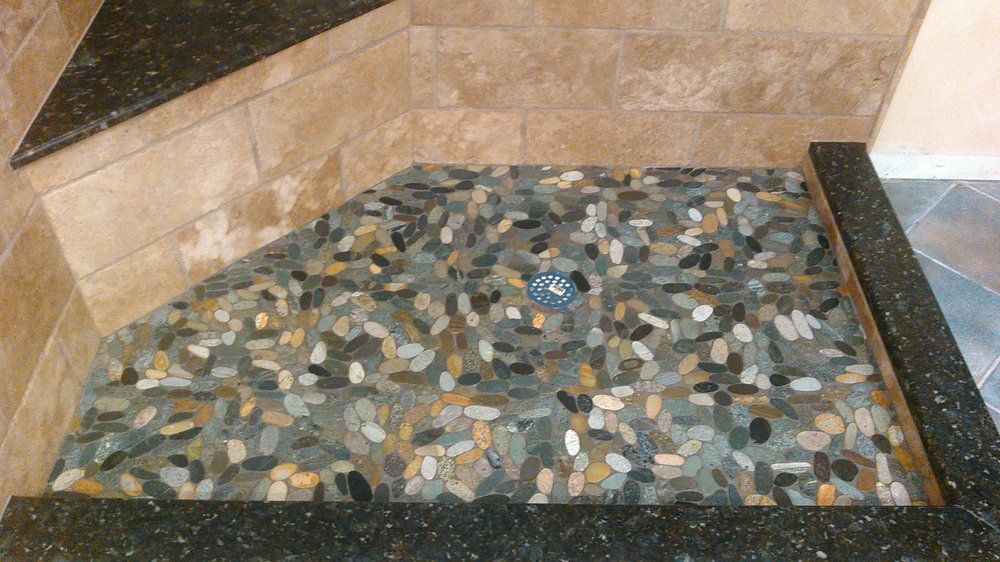 A shower stall with a tiled floor and a black counter top.