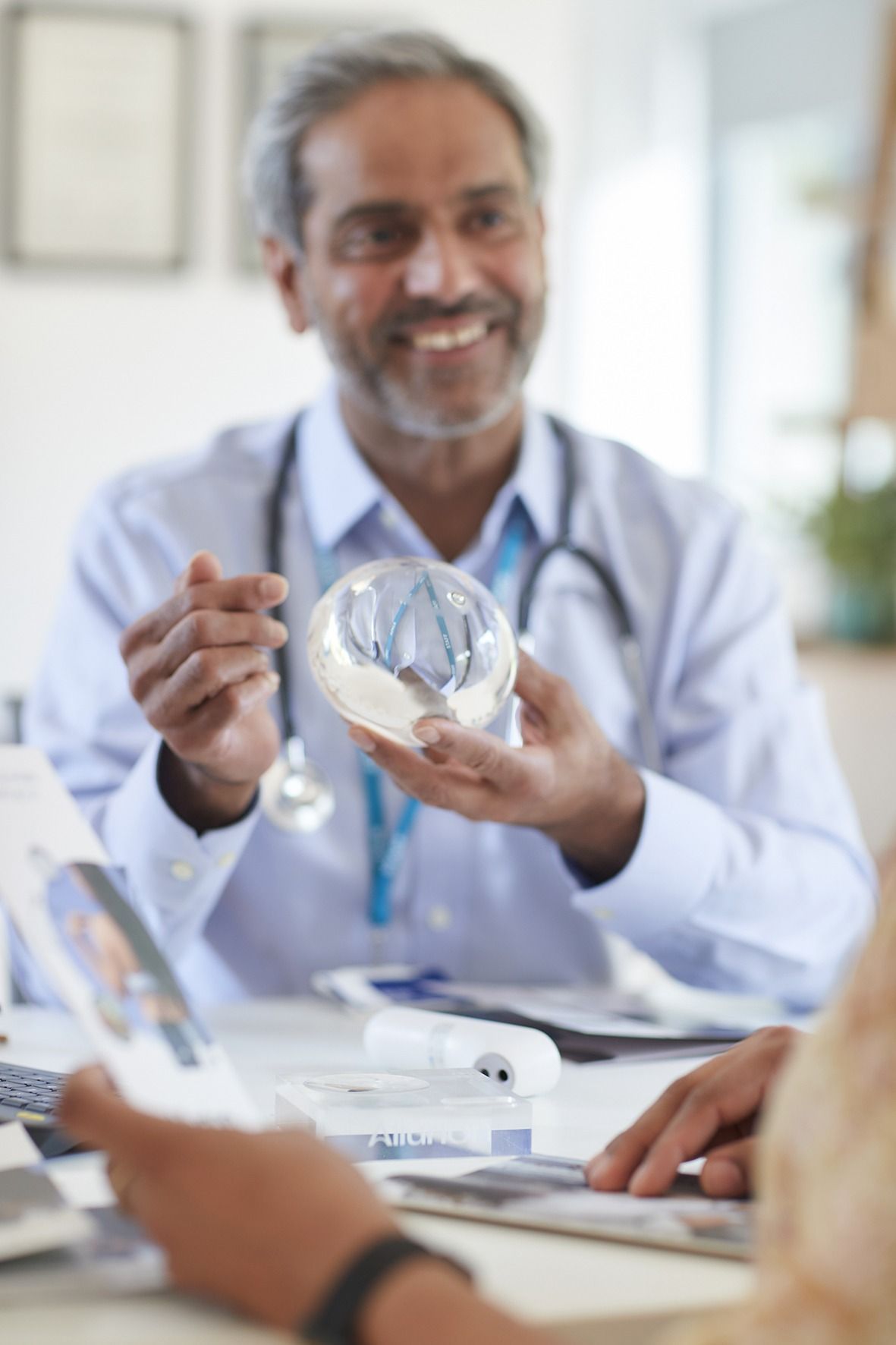 A doctor is holding a model of a heart while talking to a patient.