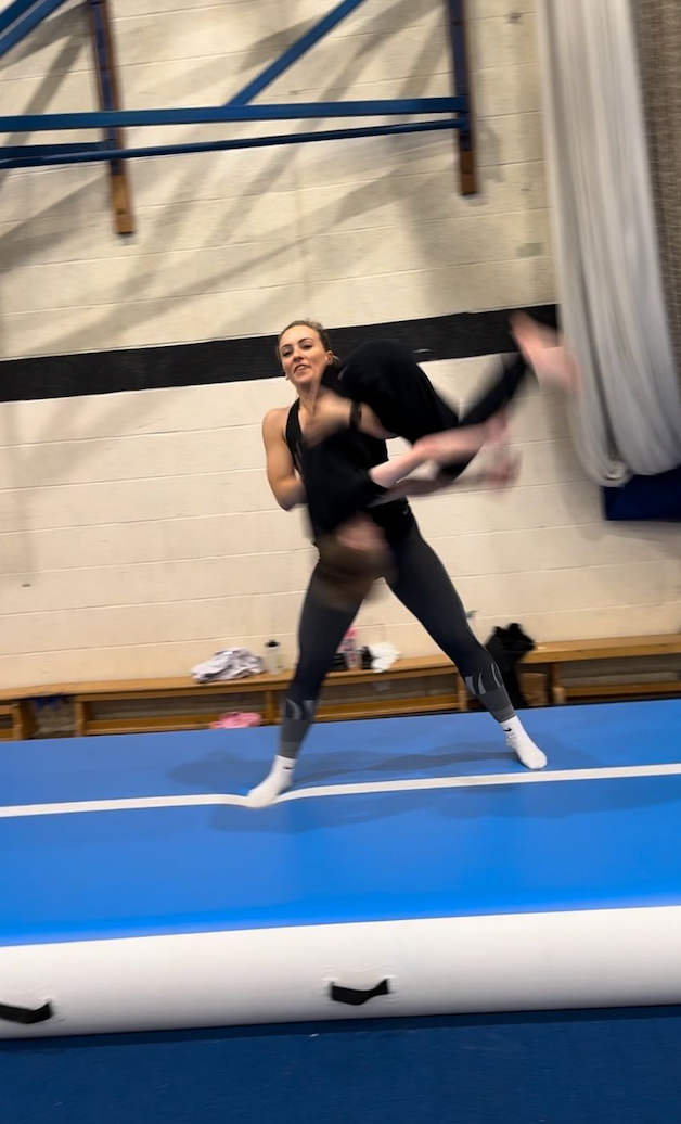A woman is doing a trick on a blue mat in a gym.